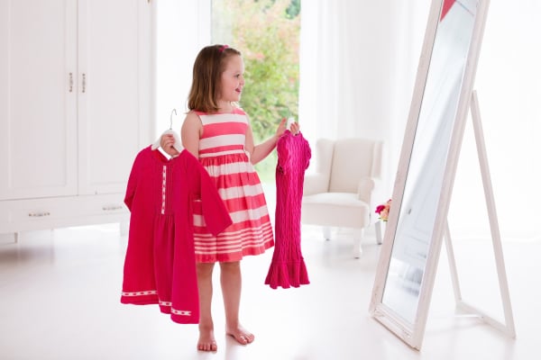 Little girl choosing dresses in white bedroom