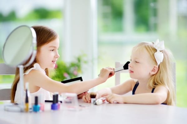 Two cute funny sisters applying make-up on sunny summer day at home