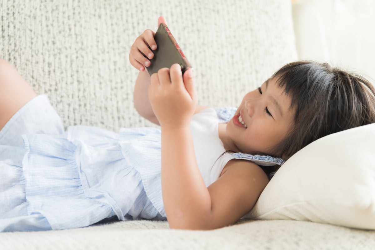 Cute little girl having fun to play game on smart phone lying on