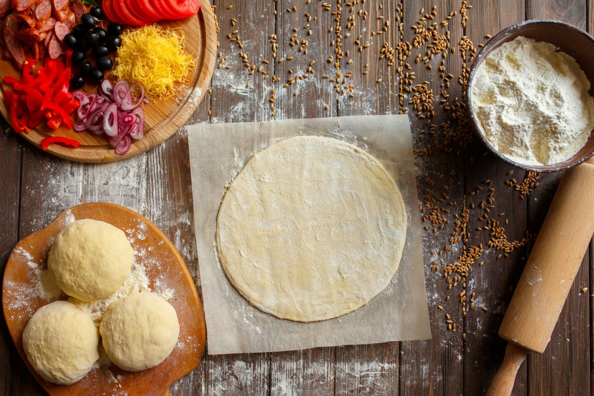 Pizza dough with ingredients on wood