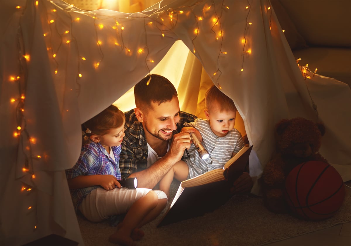 happy family father and children reading a book  in  tent at home