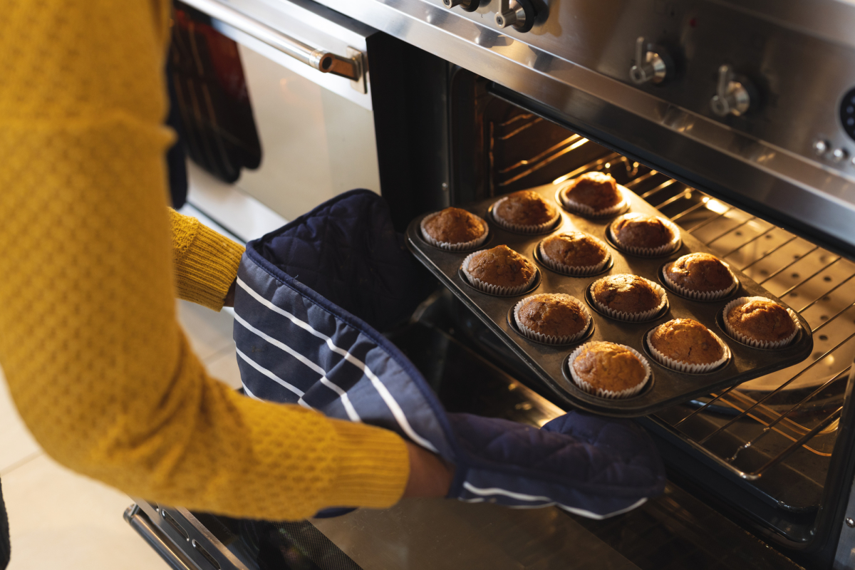 Image of midsection of african american senior woman taking out cupcakes from oven. Lifestyle, baking and spending time at home concept.